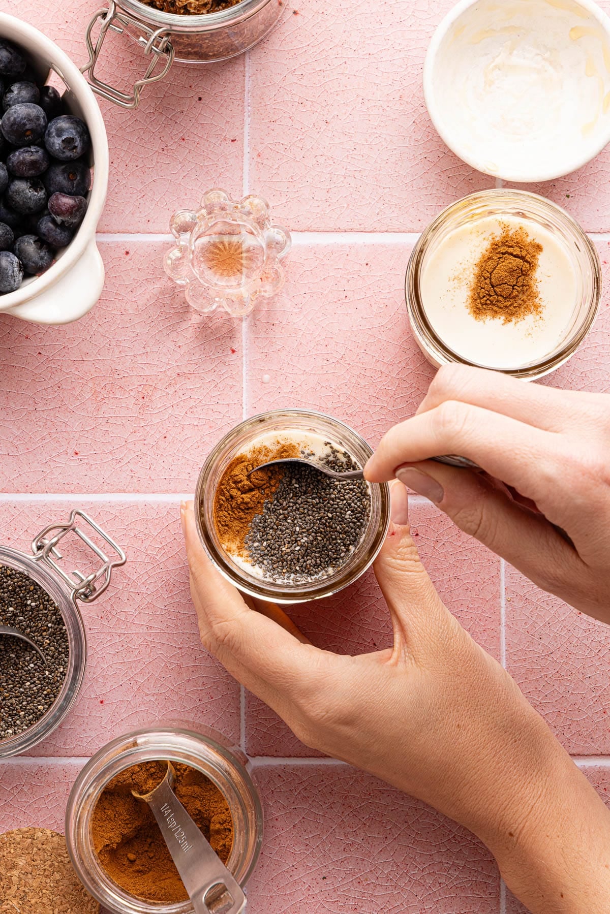 The chia seeds, oat milk, honey, vanilla, and cinnamon divided into two glass jars. A spoon is starting to mix the ingredients in the jar.