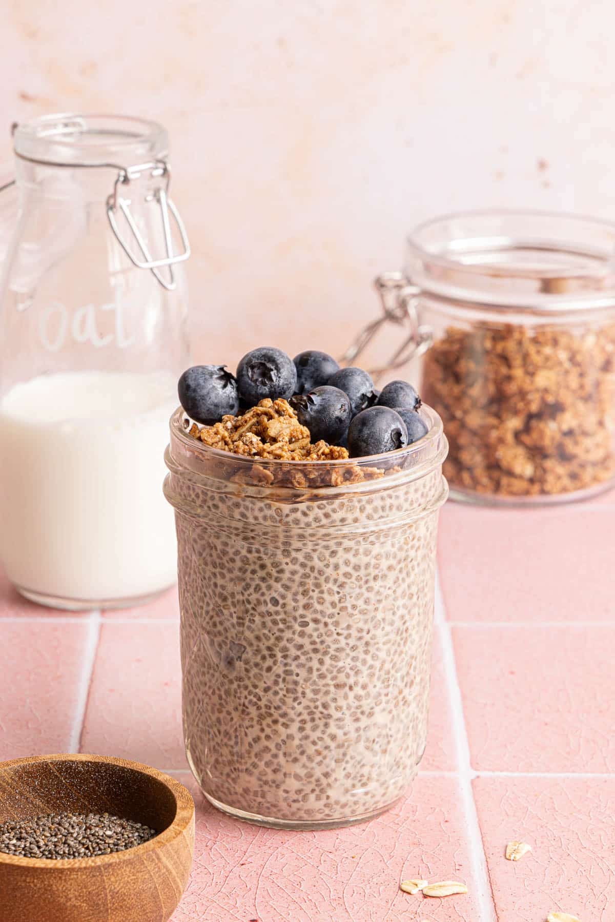 A jar filled with oat milk chia pudding topped with granola and blueberries.