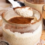 A spoon with a spoonful of tiramisu pudding over a bowl filled with the pudding.