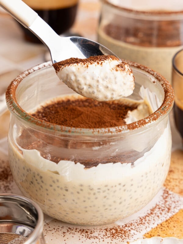A spoon with a spoonful of tiramisu pudding over a bowl filled with the pudding.