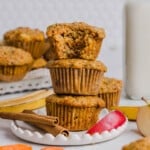 Three ABC muffins (apple, carrot, and banana) stacked on a plate. A bits is taken out of the top muffin to show the inside texture.