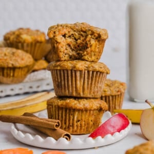 Three ABC muffins (apple, carrot, and banana) stacked on a plate. A bits is taken out of the top muffin to show the inside texture.