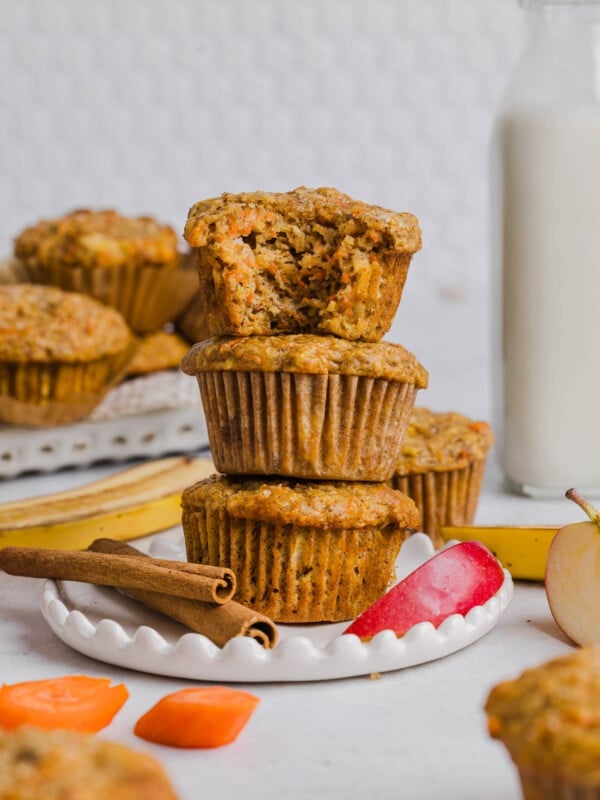 Three ABC muffins (apple, carrot, and banana) stacked on a plate. A bits is taken out of the top muffin to show the inside texture.