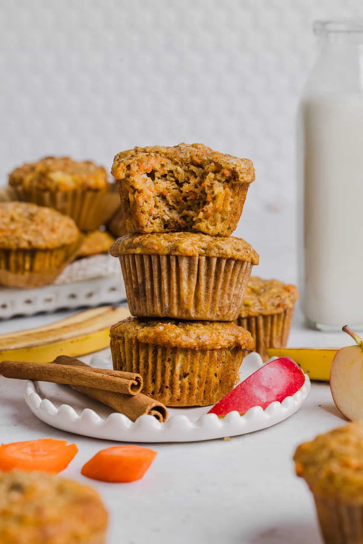 Three ABC muffins (apple, carrot, and banana) stacked on a plate. A bits is taken out of the top muffin to show the inside texture.