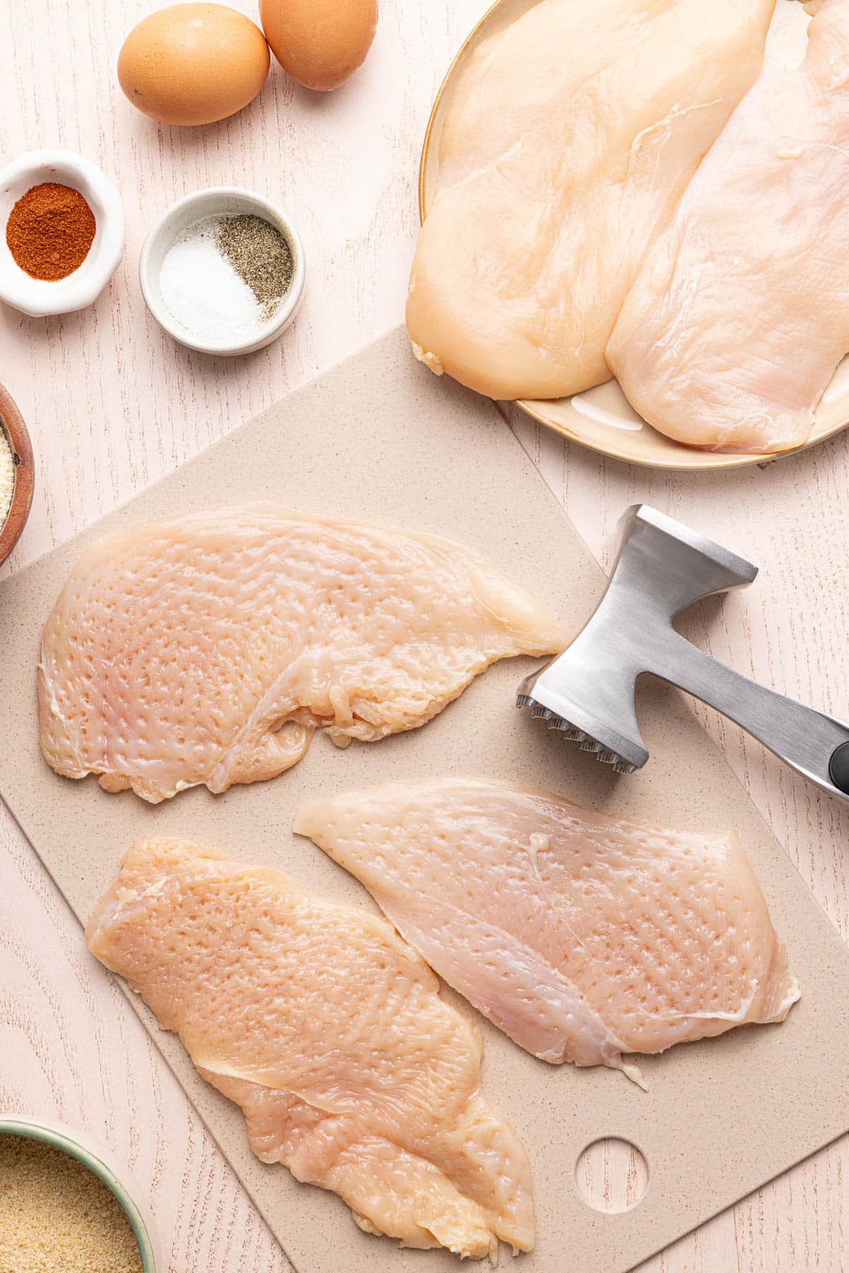 The chicken cutlets pounded into thin pieces on a cutting board.