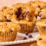 Chocolate chip muffins with cottage cheese stacked on a white serving platter with a bite taken out of the one on top.