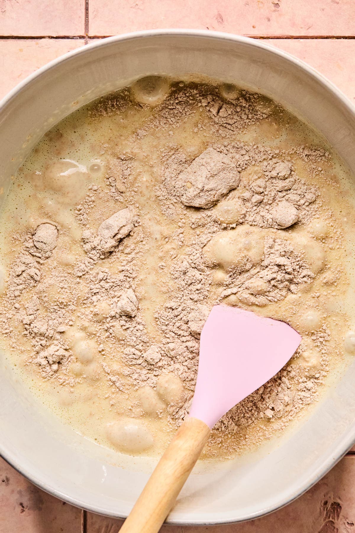 A spatula folds the dry ingredients into the wet ingredients in a large bowl.