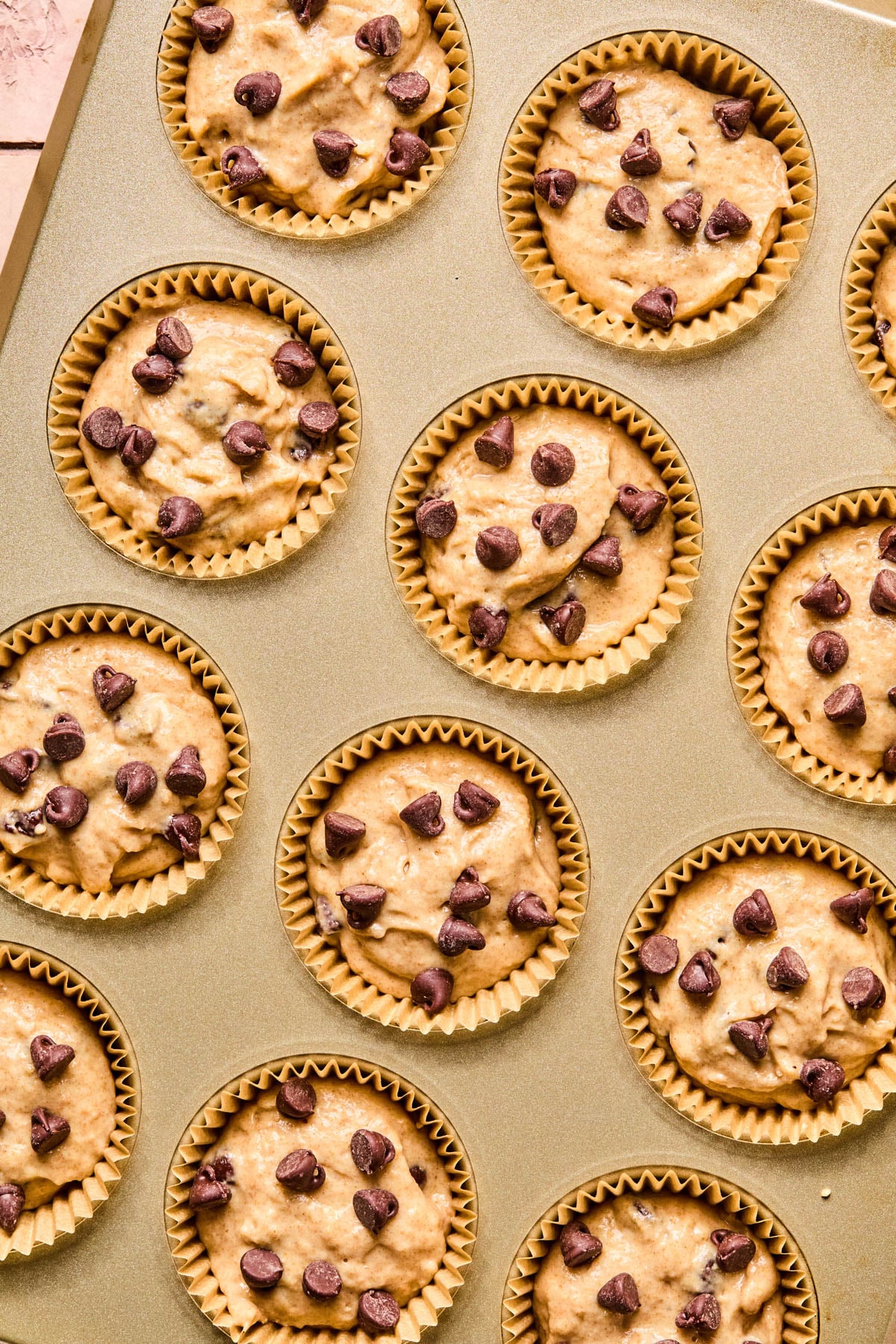 The muffin batter in lined muffin pan with extra chocolate chips sprinkled on top.