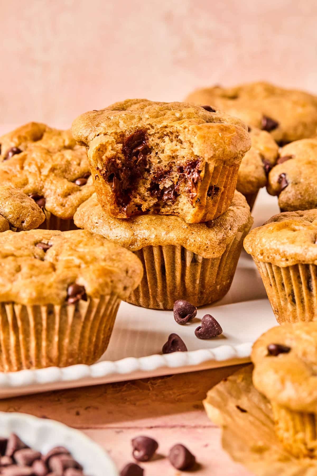 Chocolate chip muffins with cottage cheese stacked on a white serving platter with a bite taken out of the one on top.