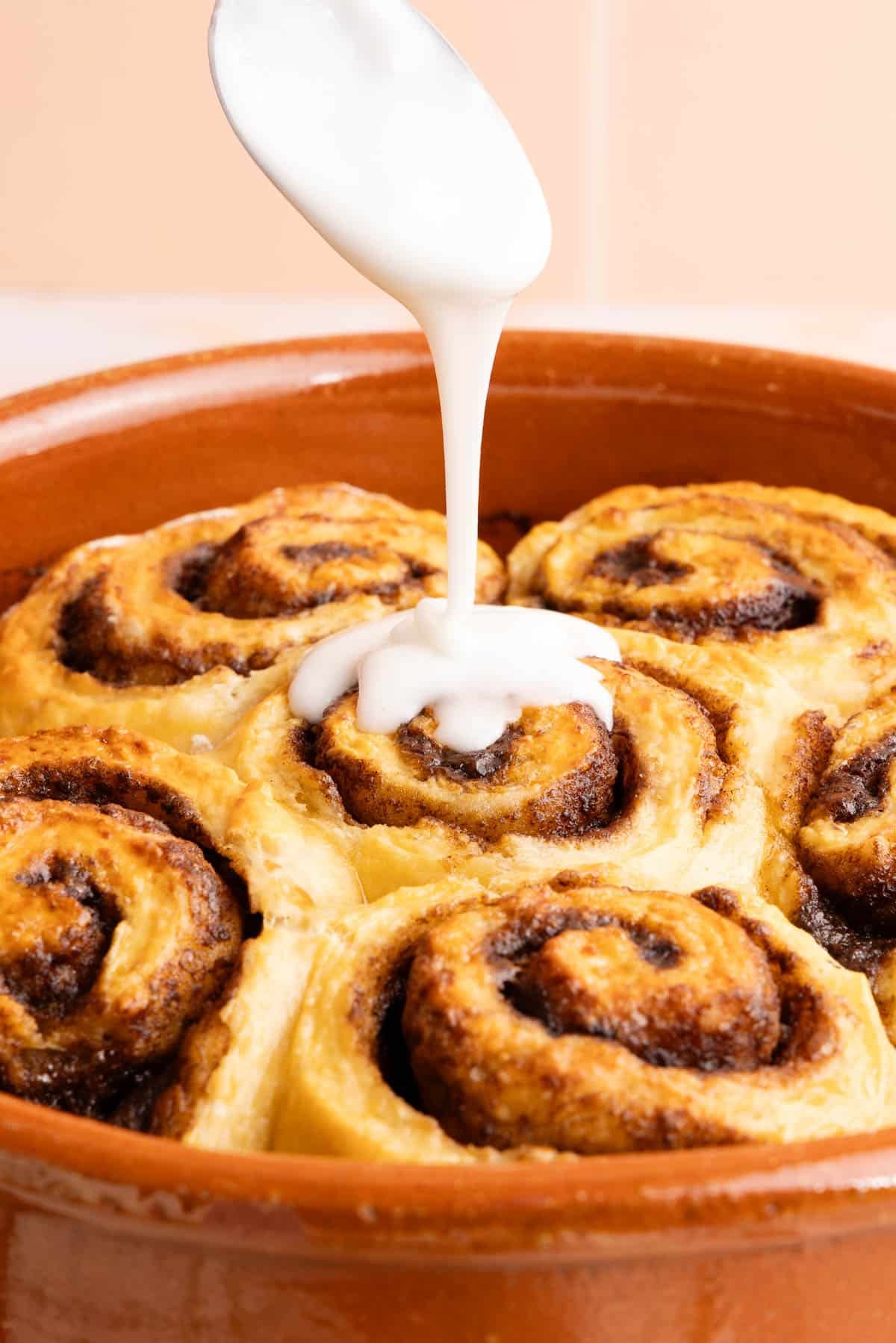 A spoon drizzles the glaze over the baked cream cheese cinnamon rolls.
