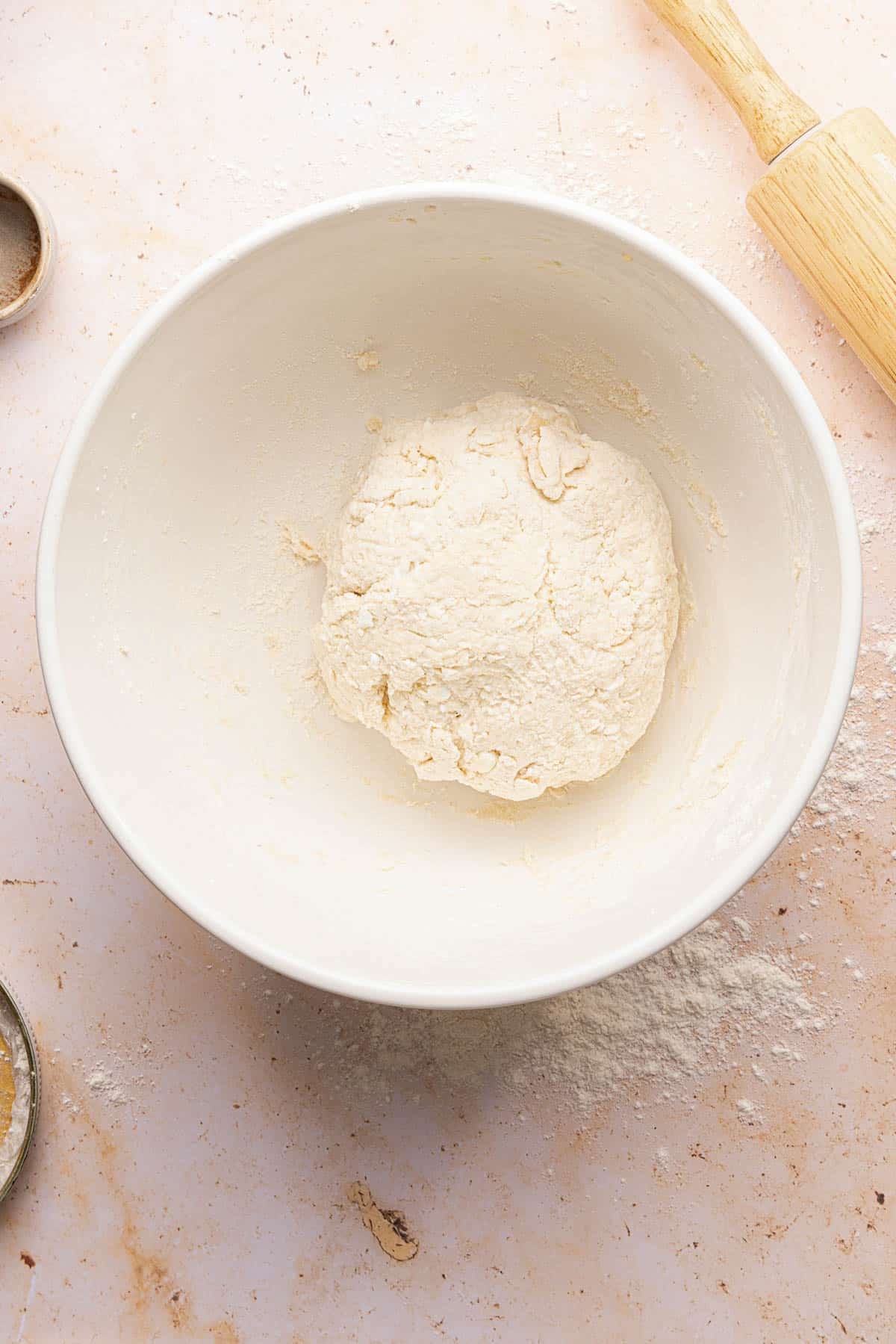 The ball of dough in a white bowl on the countertop.