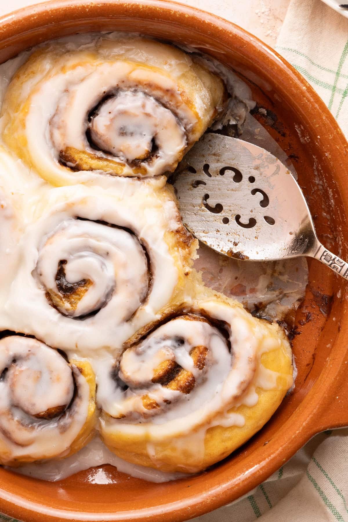 A serving utensils sits in the baking with five cinnamon rolls, the remaining cinnamon roll is removed from the dish.