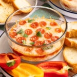 A cottage cheese pizza bowl on a serving plate with sliced peppers and crostini for serving.