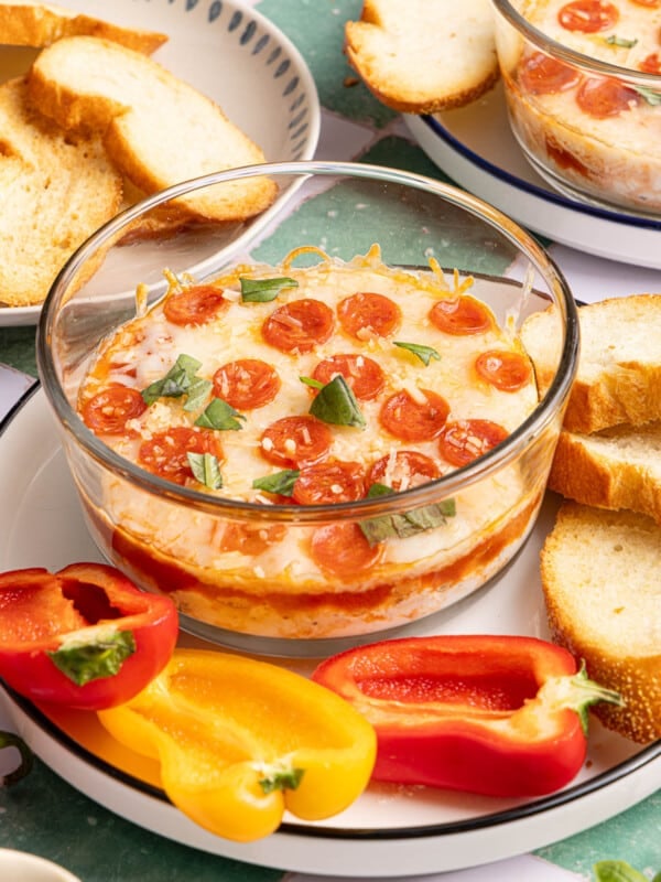 A cottage cheese pizza bowl on a serving plate with sliced peppers and crostini for serving.