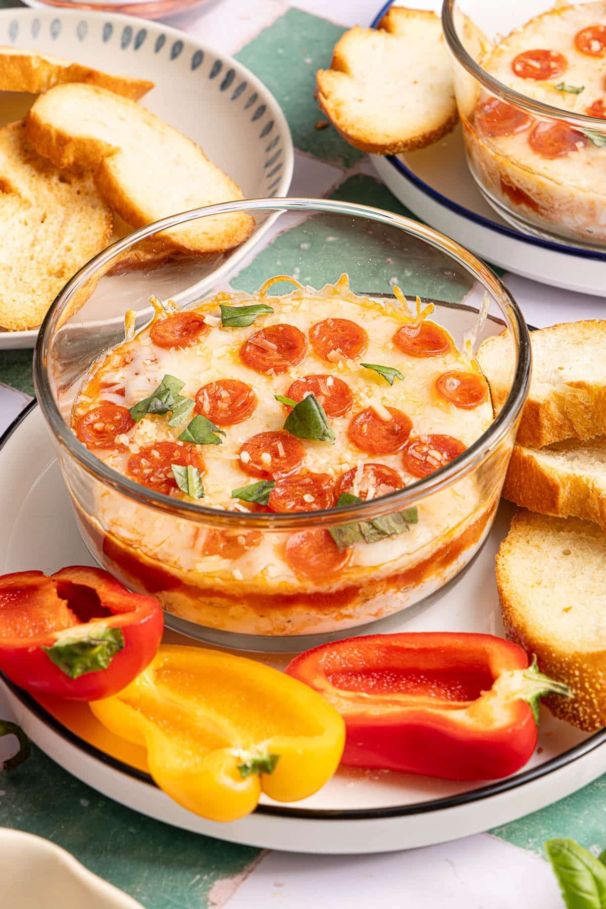 A cottage cheese pizza bowl on a serving plate with sliced peppers and crostini for serving.