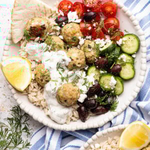 A bowl with the rice, meatballs, cucumbers, olives, tomatoes and sauce for serving.