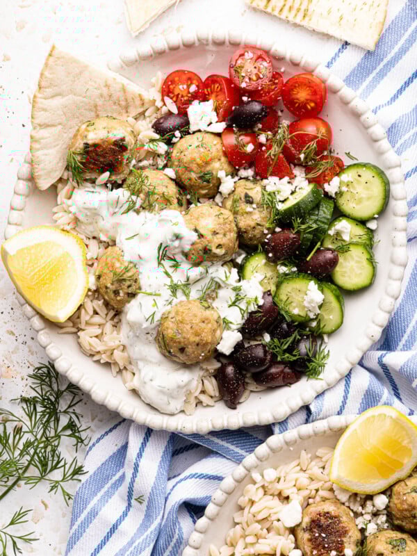 A bowl with the rice, meatballs, cucumbers, olives, tomatoes and sauce for serving.