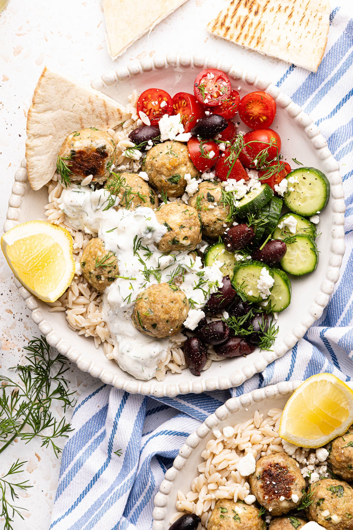 A bowl with the rice, meatballs, cucumbers, olives, tomatoes and sauce for serving.