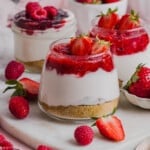 Three High Protein Cheesecake Jars sitting on a marble serving platter with fresh raspberries and strawberries on the side.