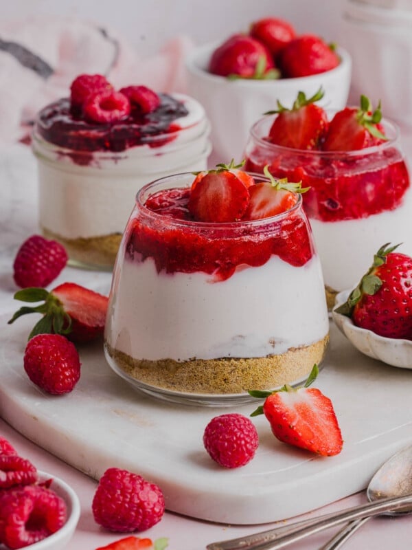 Three High Protein Cheesecake Jars sitting on a marble serving platter with fresh raspberries and strawberries on the side.