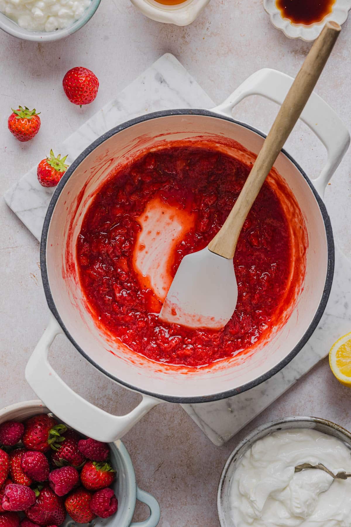 The mashed strawberry jam-like mixture in a saucepan with a spatula for mashing.