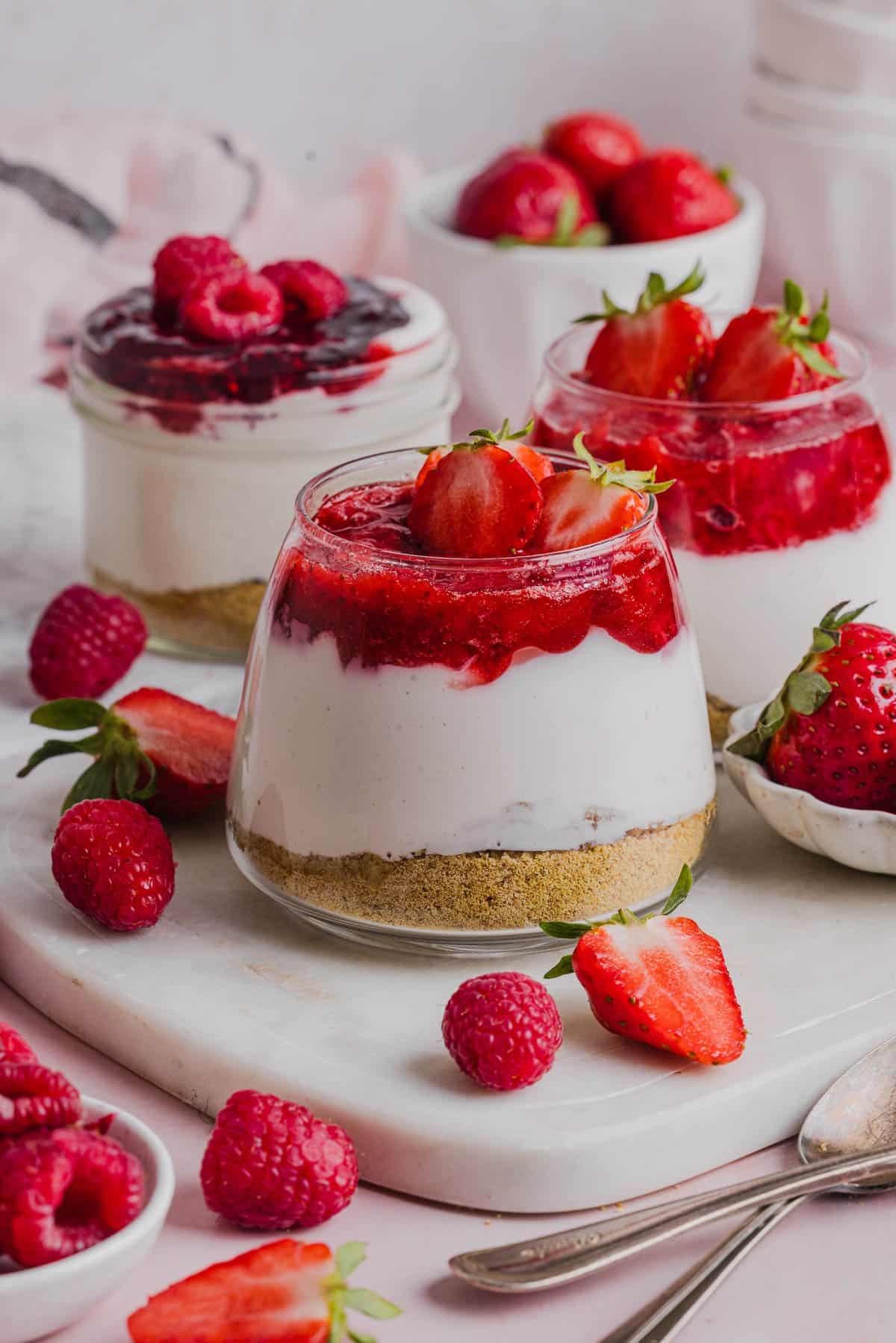 Three High Protein Cheesecake Jars sitting on a marble serving platter with fresh raspberries and strawberries on the side.