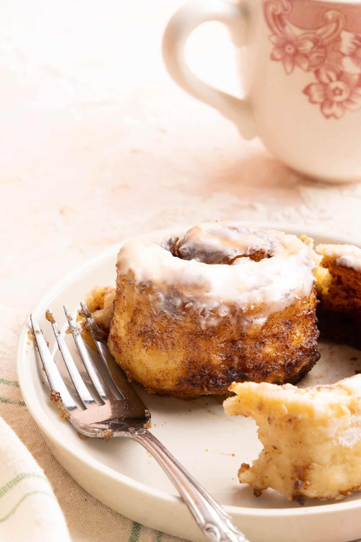 An unwrapped cinnamon roll on a plate with a fork.