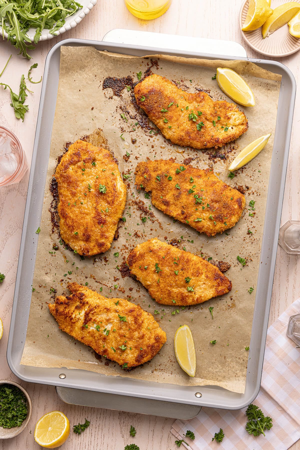 Five baked chicken cutlets on a baking sheet after baking.