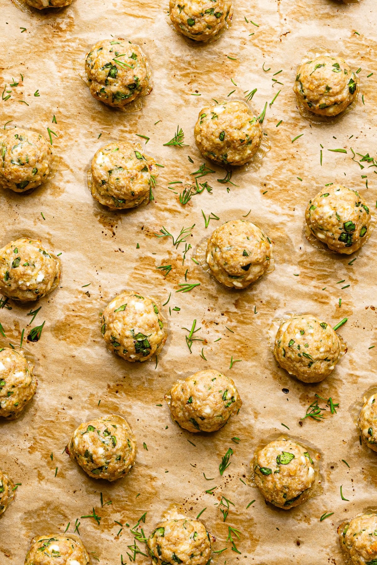 The baked turkey feta meatballs on parchment paper on the baking sheet after baking.