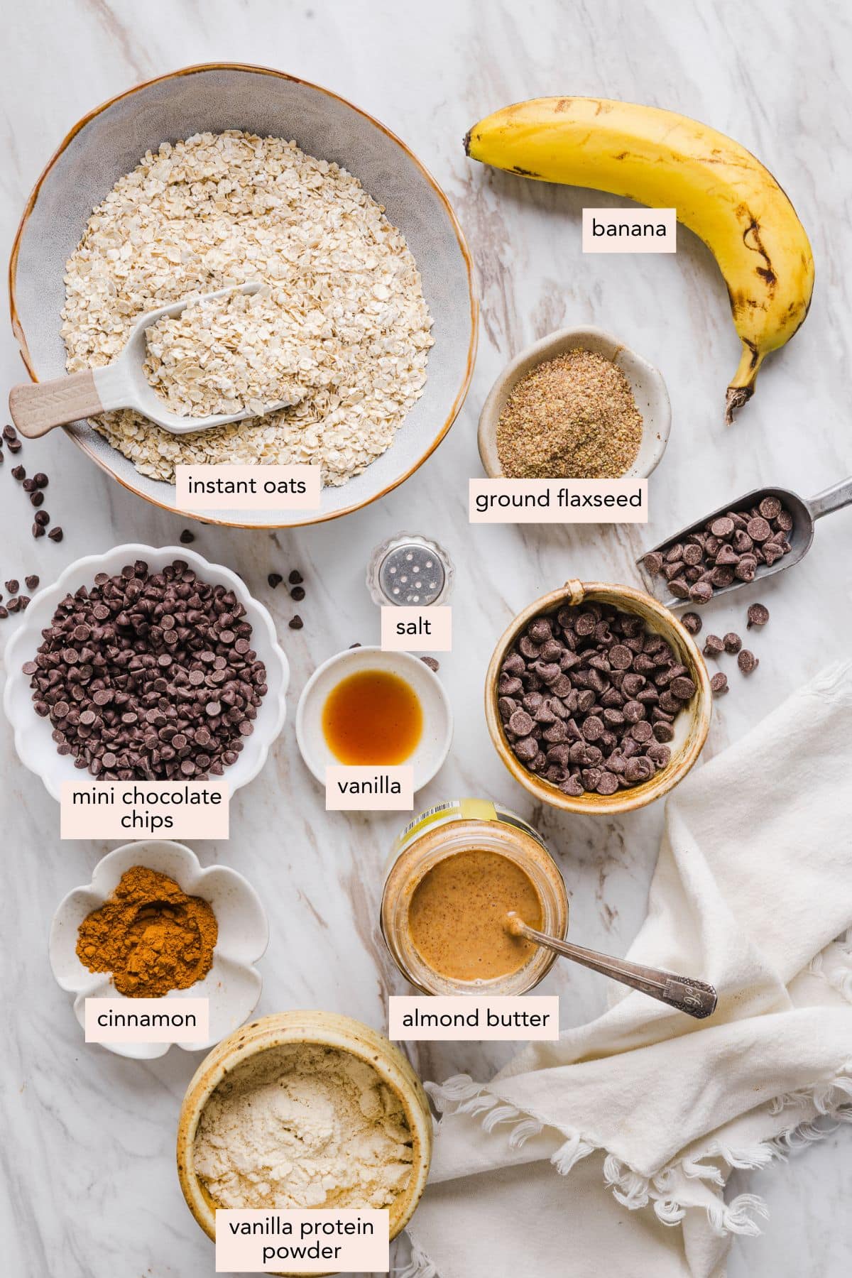 All of the ingredients for banana protein balls in bowls on a white countertop.
