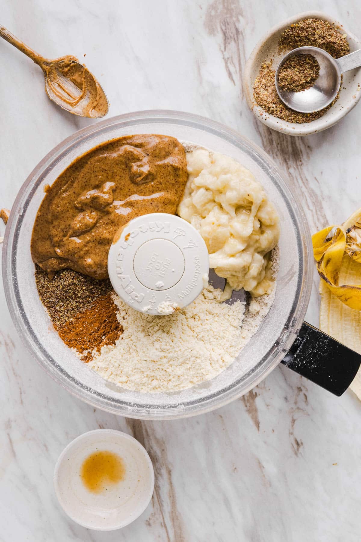 The protein powder, flax seeds, banana, almond butter, vanilla, cinnamon, and salt in the food processor with the blended oats.
