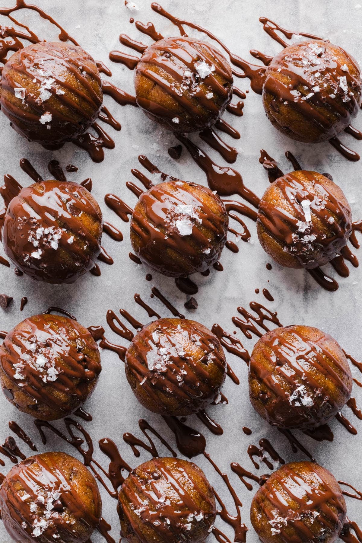 The protein balls with chocolate drizzle on top on a lined baking sheet.