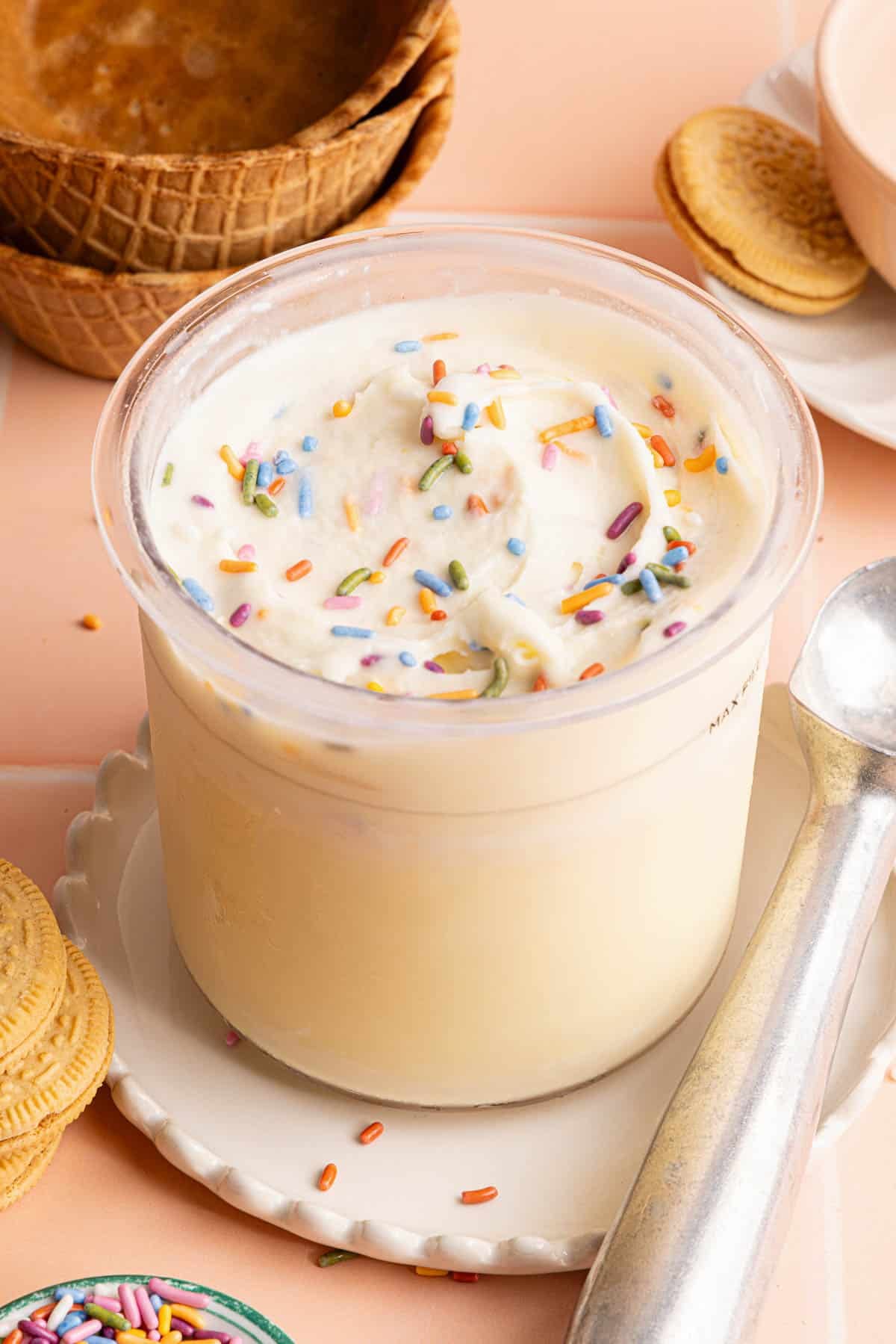 The finished cake batter ice cream with sprinkles on top sitting on a countertop with an ice cream scoop on the side.