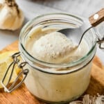 A spoon scoops some of the greek yogurt caesar dressing from a jar before drizzling over a salad.