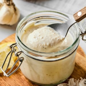 A spoon scoops some of the greek yogurt caesar dressing from a jar before drizzling over a salad.