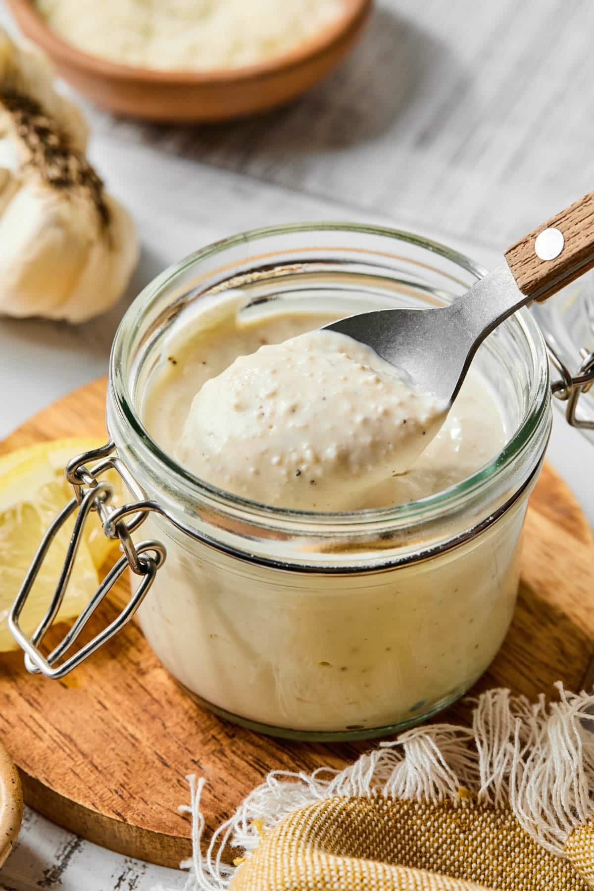A spoon scoops some of the greek yogurt caesar dressing from a jar before drizzling over a salad.