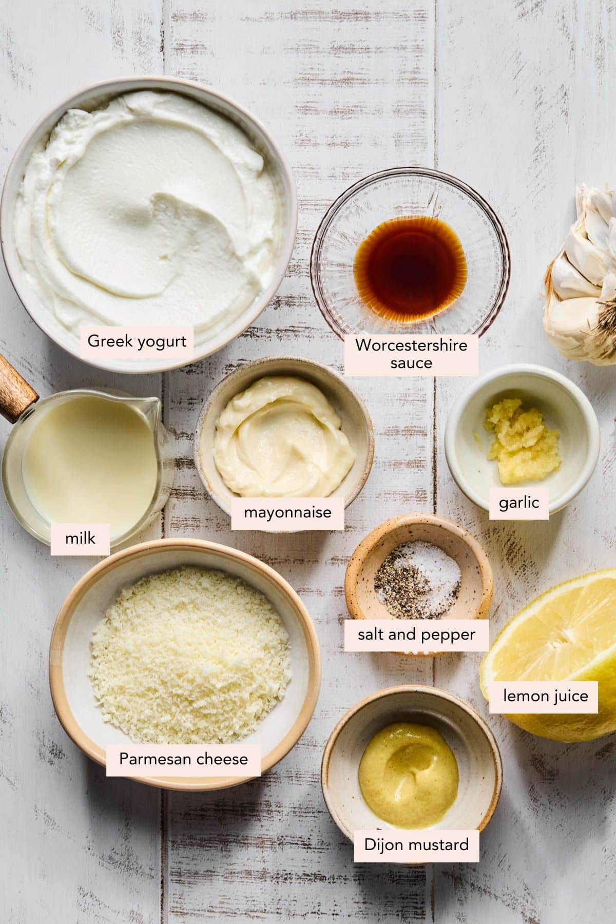 All of the ingredients for greek yogurt caesar dressing in bowls on a countertop.