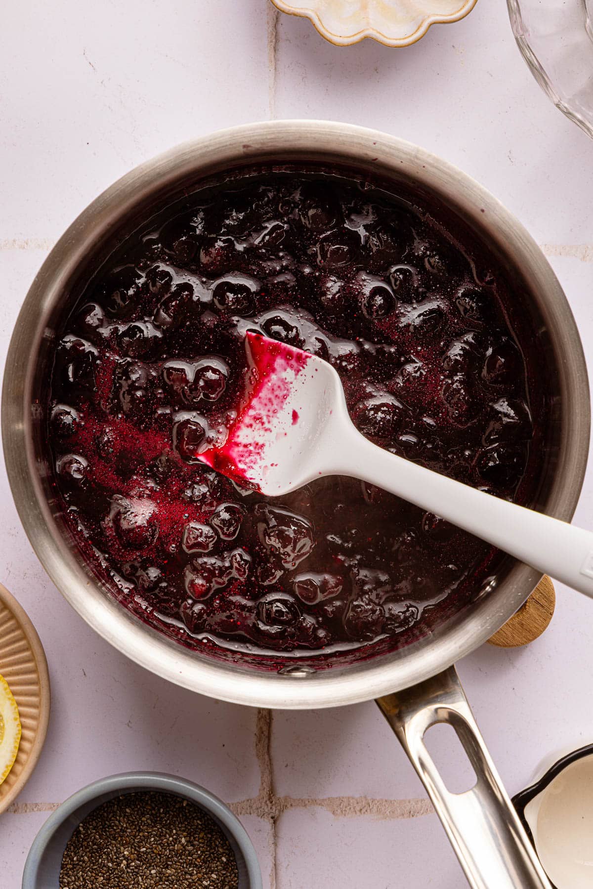 A rubber spatula mashes the blueberries in the pan.