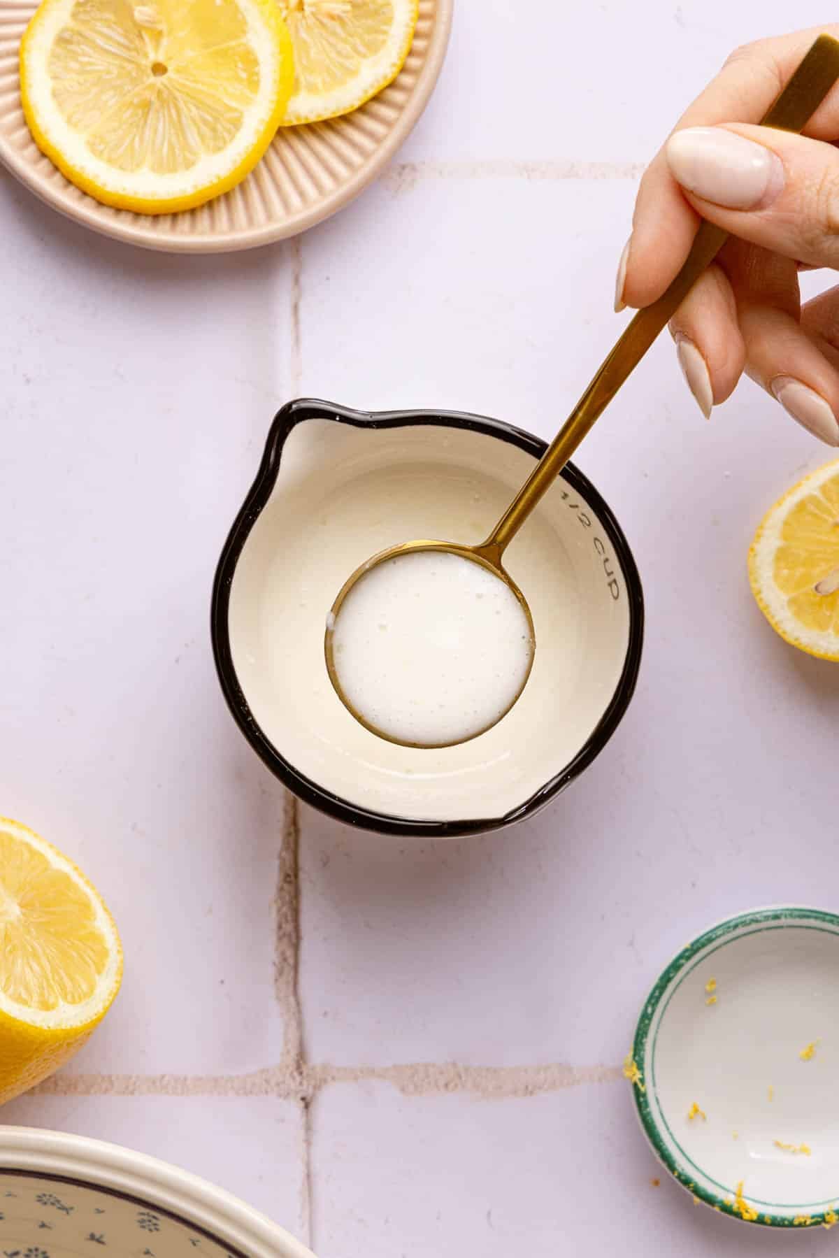 A spoon lifts the lemon glaze in a measuring cup.