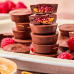 Peanut butter and jelly cups stacked on a white serving platter. One cup is split in half on top to show the insides.