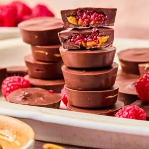 Peanut butter and jelly cups stacked on a white serving platter. One cup is split in half on top to show the insides.