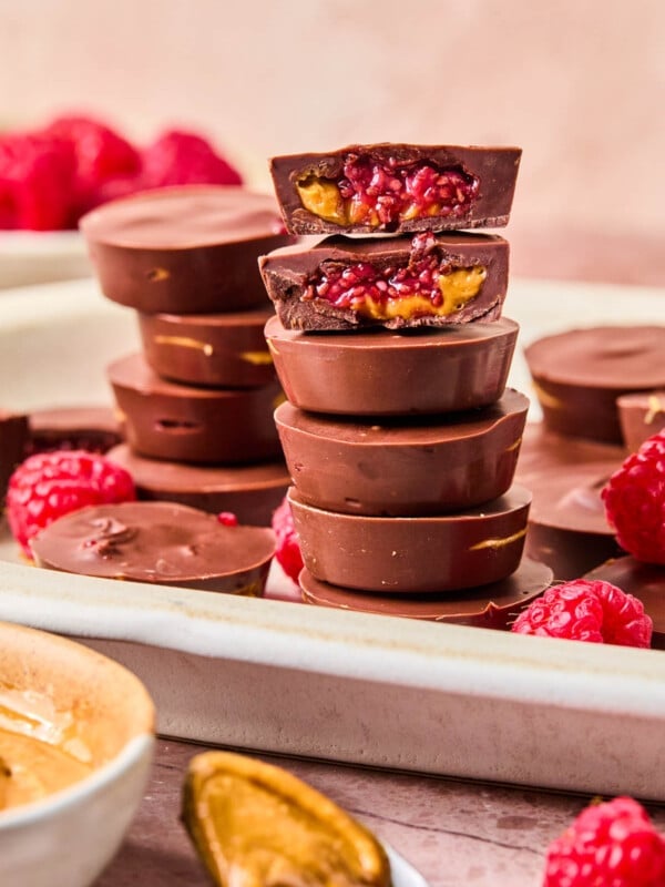 Peanut butter and jelly cups stacked on a white serving platter. One cup is split in half on top to show the insides.