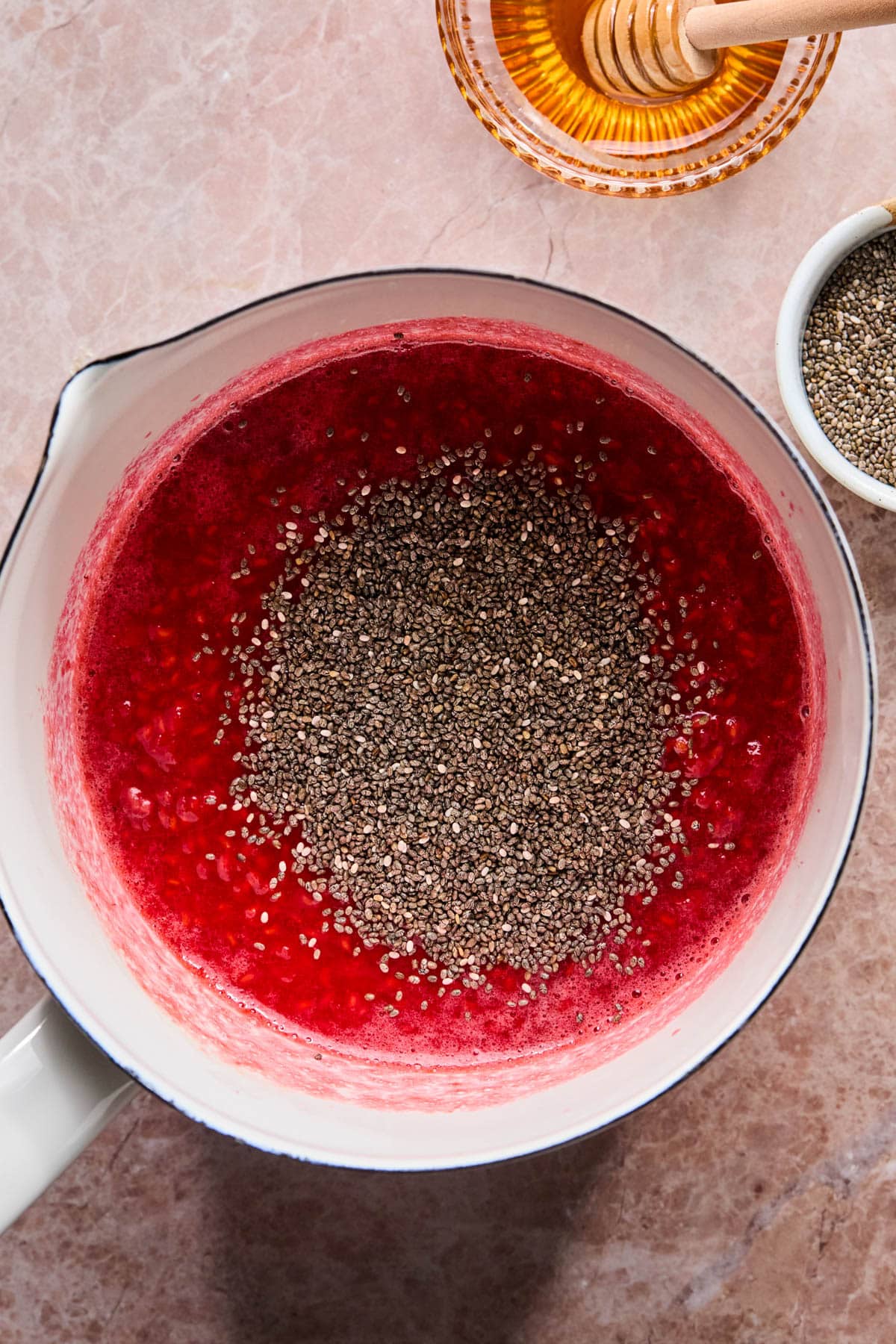 The chia seeds on top of the cooked down raspberries in the saucepan before stirring together.