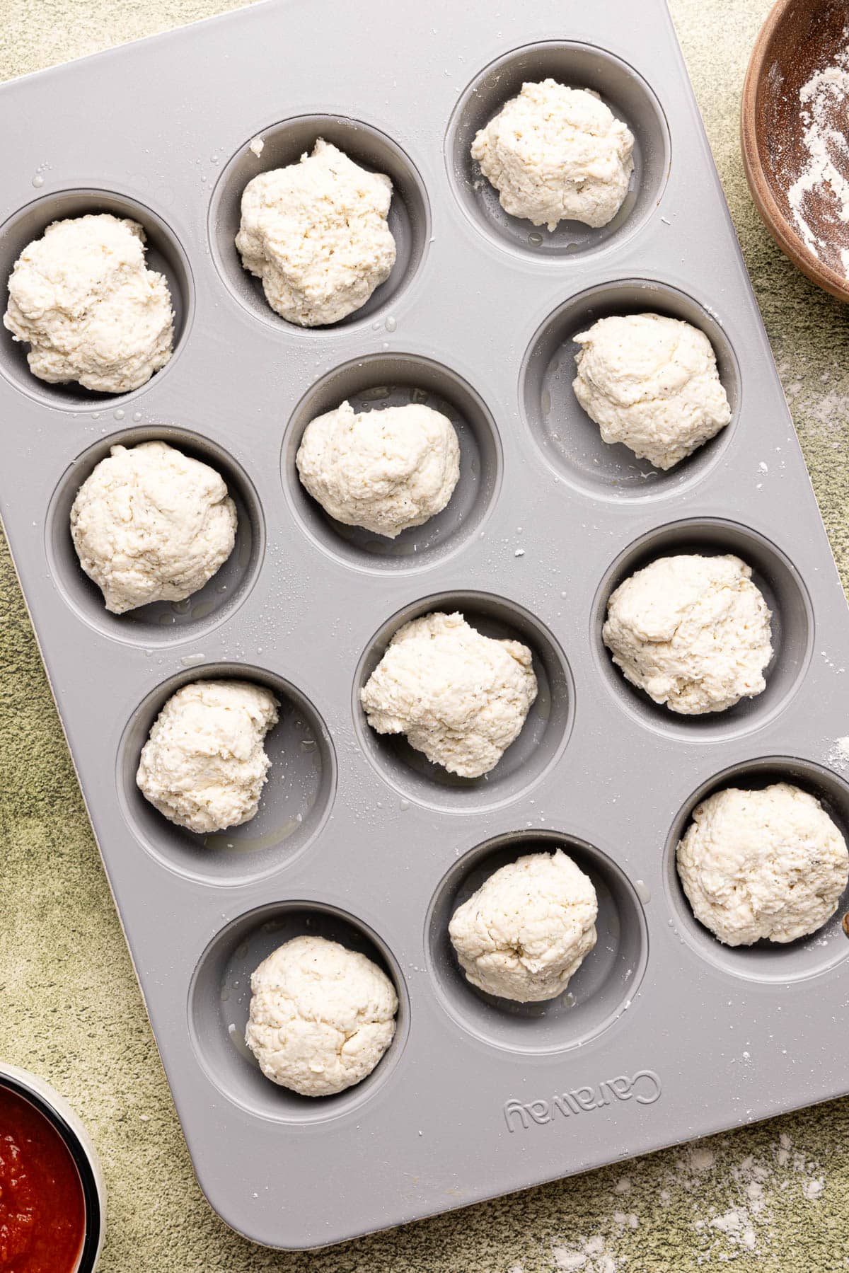 The divided dough balls in a muffin pan before pressing down in the pan.