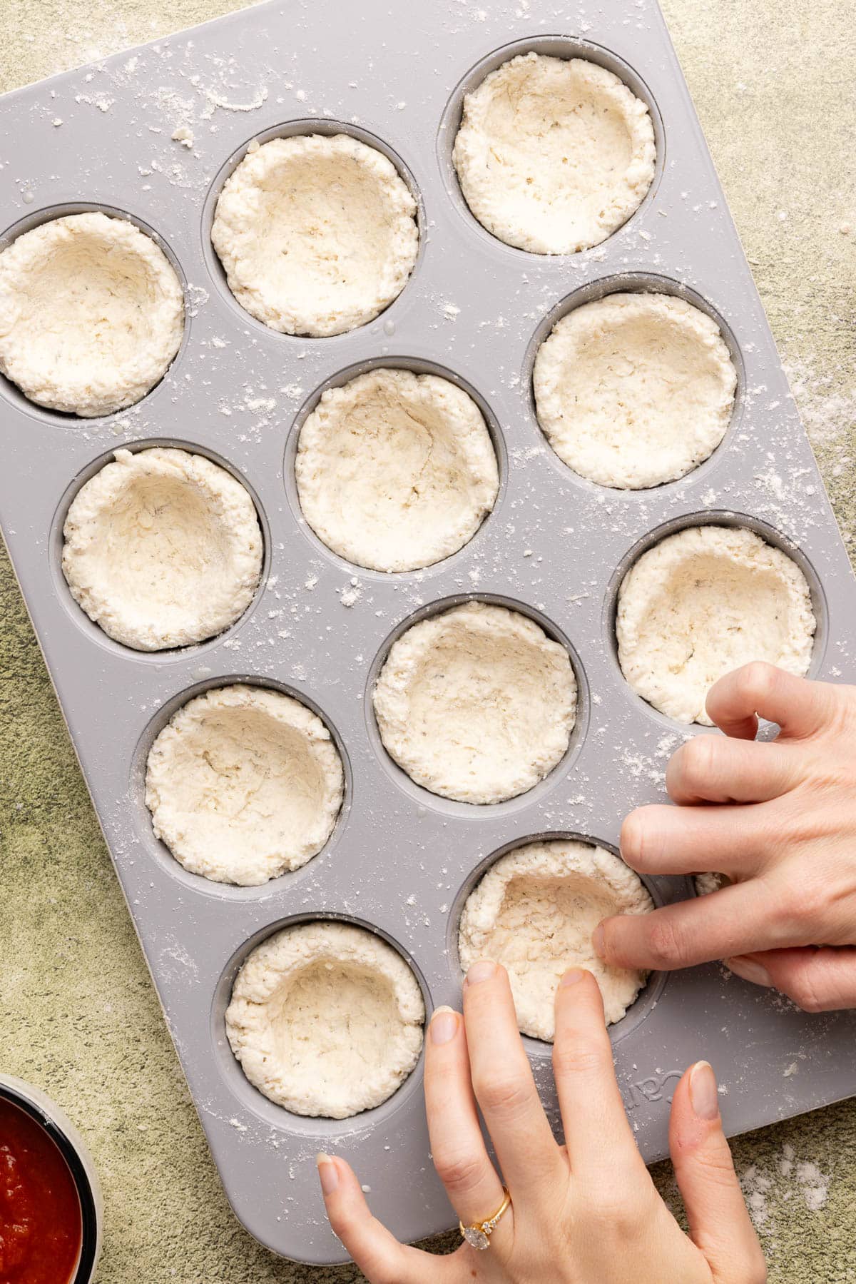 Hands pressing the dough down into the muffin cups in the muffin tin.