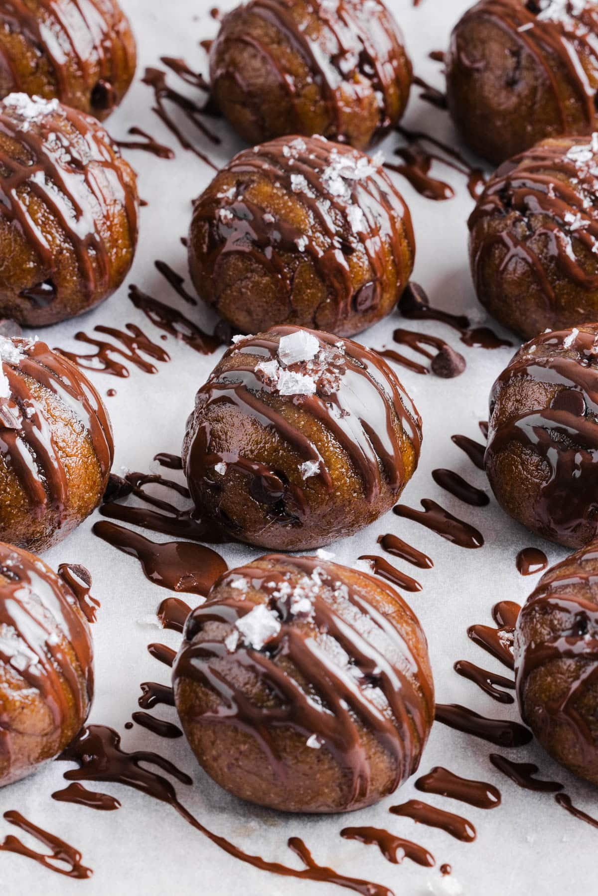 The banana protein balls with drizzled chocolate on top of a lined sheet pan.