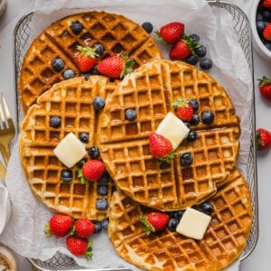Four protein waffles with slices of butter and fresh fruit on top in a mesh serving basket.
