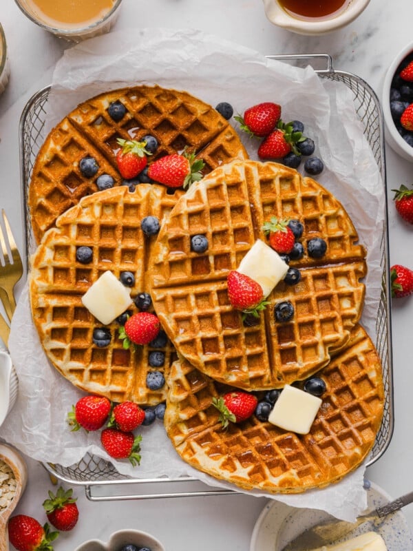 Four protein waffles with slices of butter and fresh fruit on top in a mesh serving basket.