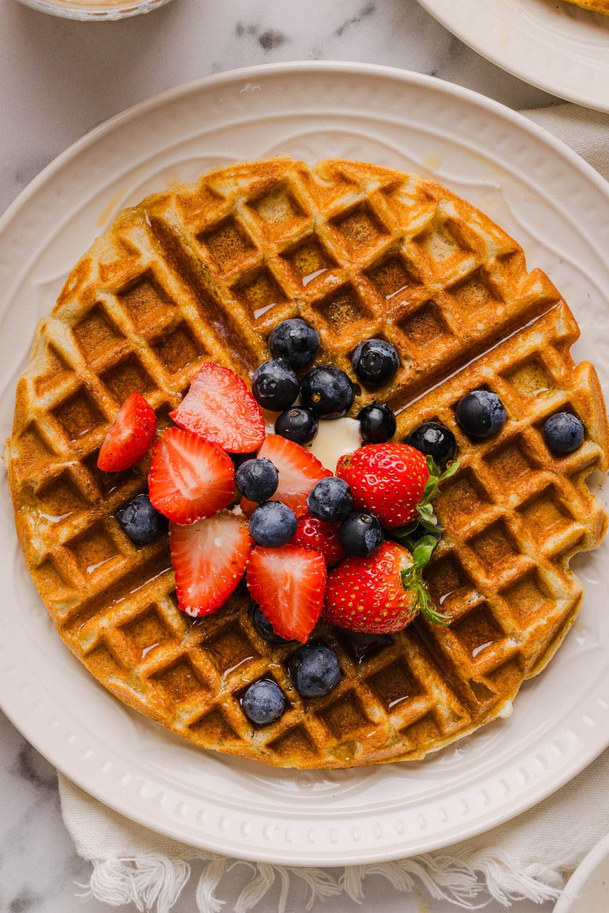 A waffle on a plate with a pat of butter and fresh blueberries and strawberries for serving.