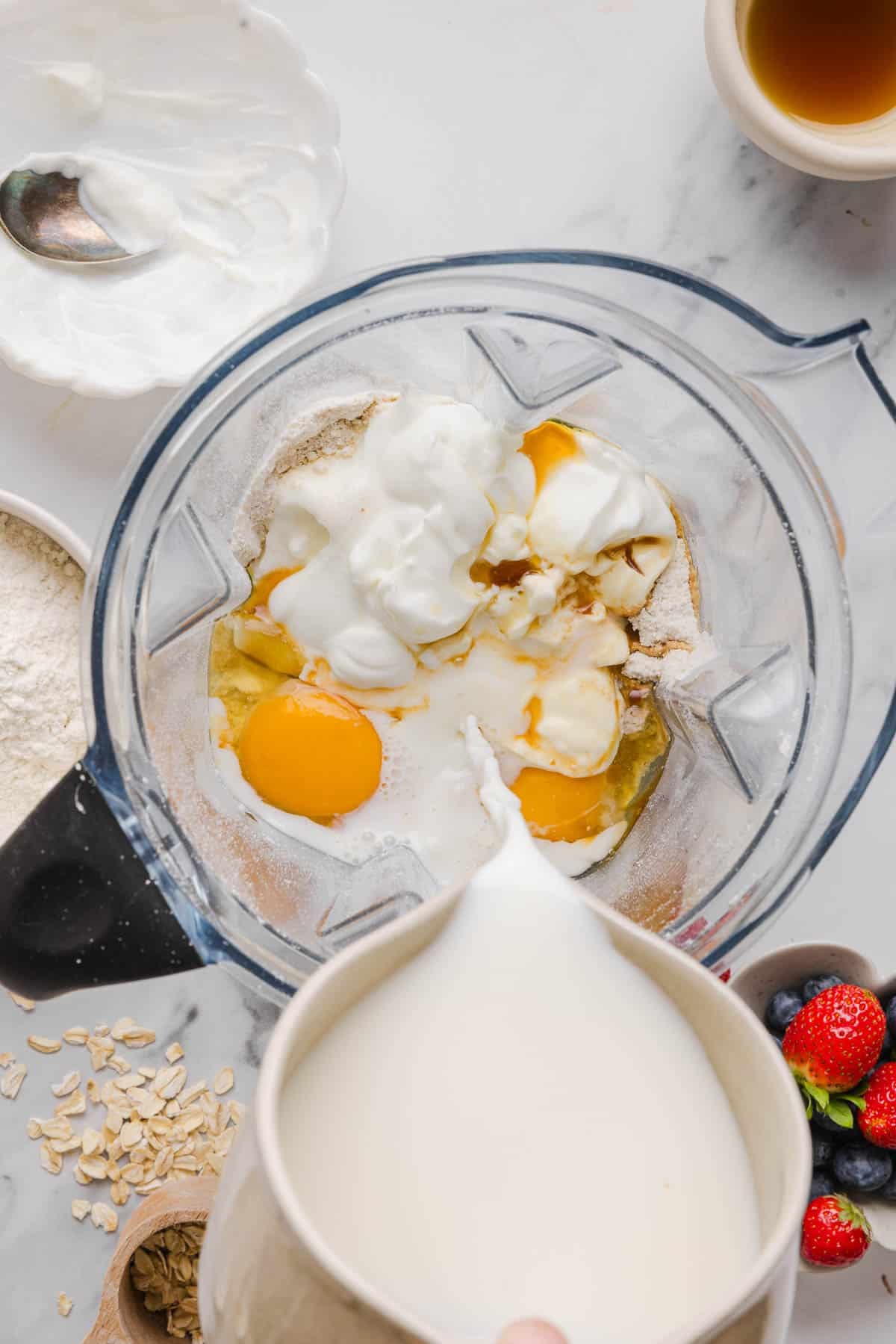 Pouring the milk into the blender with the other ingredients before blending again.
